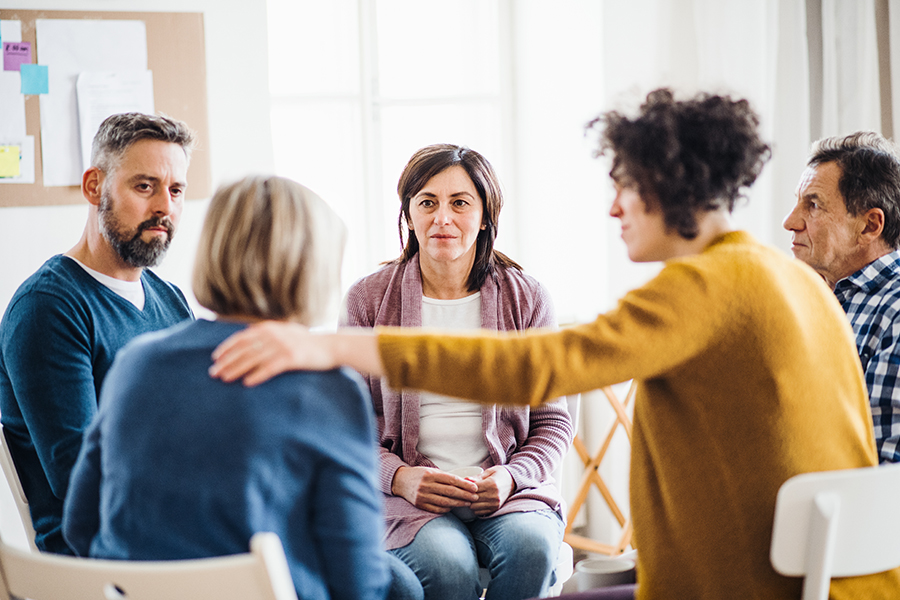 Men and women sitting in a circle during group therapy, supporting each other. - Florida Addiction Centers